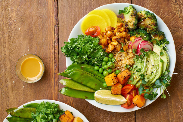 Healthy vegetarian lunch bowls with avocado and chickpeas with quinoa and vegetables garnished with microgreens and nut dressing  on wooden background - Photo, image