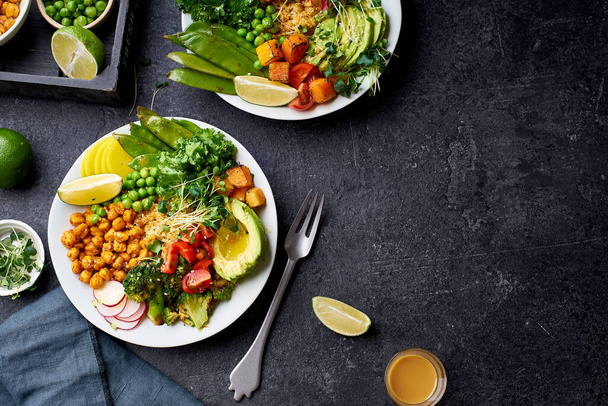 Healthy vegetarian lunch bowls with avocado and chickpeas with quinoa and vegetables garnished with microgreens and nut dressing  on dark concrete background - 写真・画像