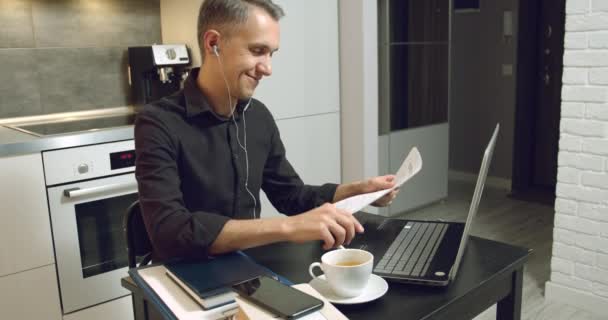 Young business man having video chat with customers or partners discussing a contract or report using headphones and laptop at home - Filmati, video