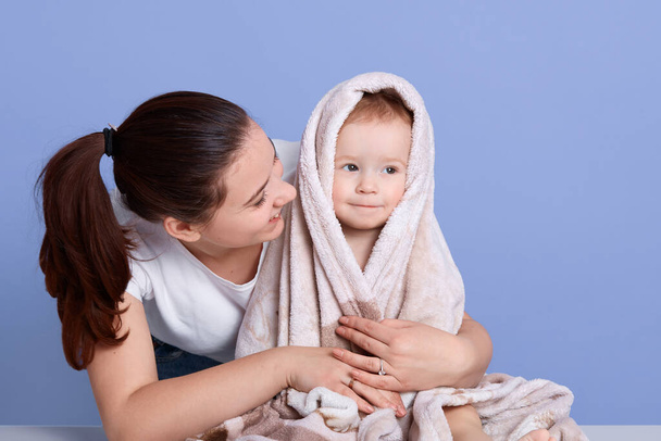 Horizontal shot of mommy and her little son wrapped in towel after bathing, young adorable mother being photographed with baby boy after washing, lady looking at child with love. Parenthood concept. - Photo, Image