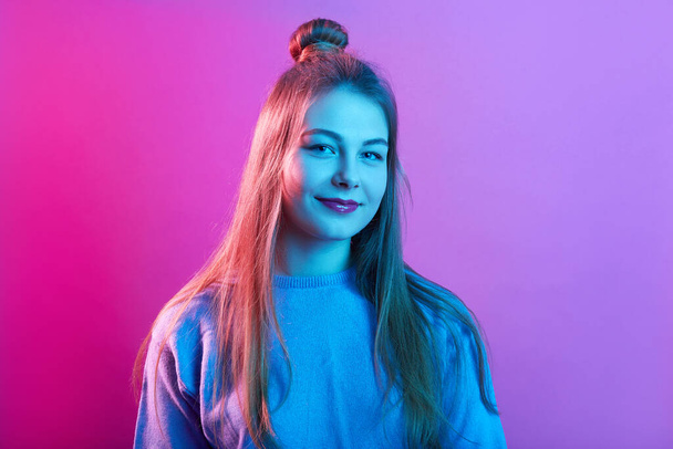 Closeup portrait of young teenager female wearing casual sweater, posing with hair bun, looking smiling directly at camera, posing isolated over pink neon background. People lifestyle concept. - Valokuva, kuva