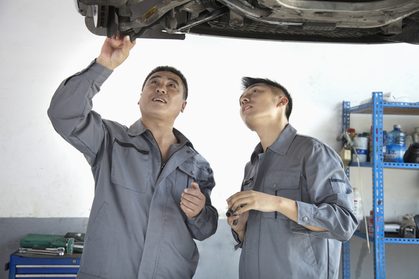 zwei Mechaniker betrachten die Unterseite eines Autos - Foto, Bild