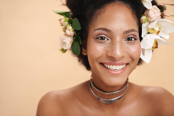 Bej arka planda saklanmış saçlarında çiçekler olan yarı çıplak Afrikalı Amerikalı bir kadının portresi. - Fotoğraf, Görsel