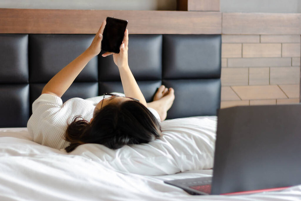 jovem mulher de negócios usando telefone móvel na cama enquanto trabalhava em casa durante a crise covid-19
. - Foto, Imagem