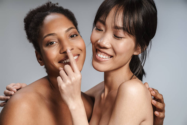 Portrait of two multinational half-naked women posing together and making fun isolated over grey background - Photo, image