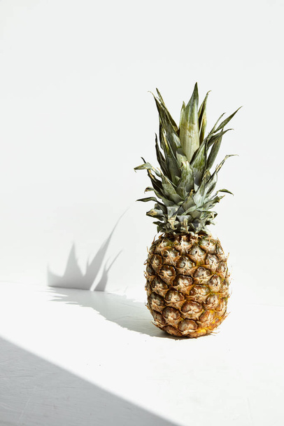 Ripe tropical pineapple fruit with green leaves and shadow on a white background. - Photo, Image