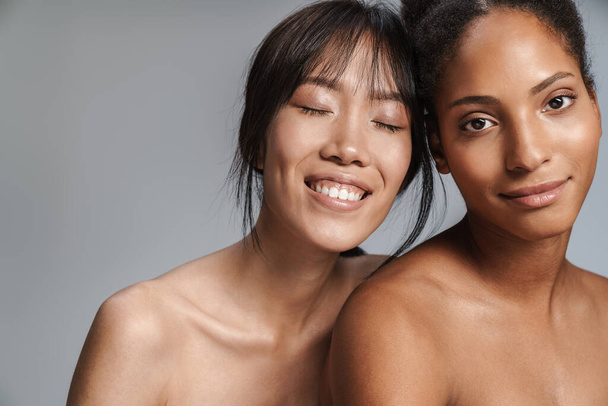 Portrait of two multinational half-naked women posing together and smiling isolated over grey background - Foto, Imagem
