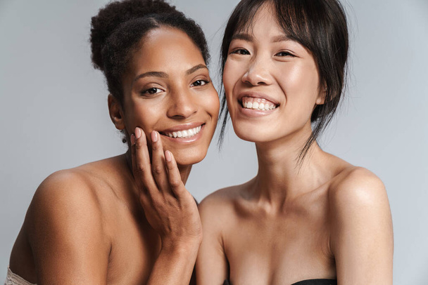 Portrait of two multinational half-naked women hugging and laughing isolated over grey background - Foto, Bild