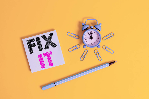 Writing note showing Fix It. Business photo showcasing Fasten something securely in a particular place or position To repair Metal alarm clock wakeup clips ballpoint notepad colored background. - Foto, afbeelding