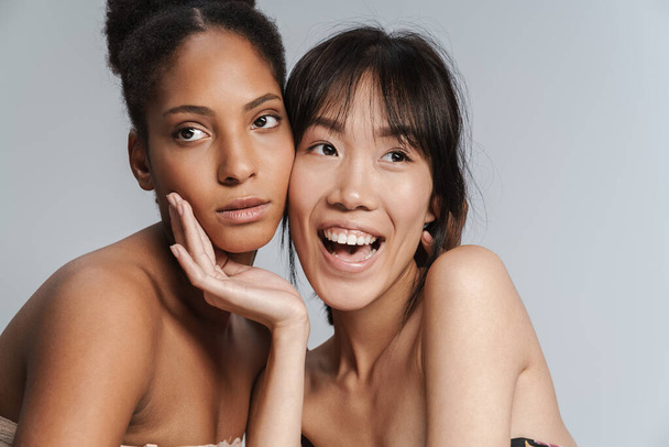 Portrait of two multinational half-naked women posing together and smiling isolated over grey background - Foto, imagen