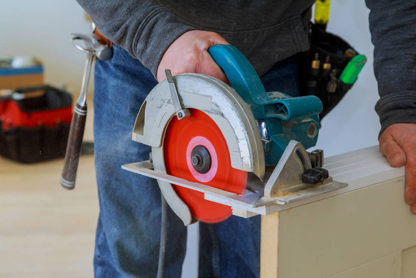 Les mains de l'homme tenant la scie circulaire et se préparant à faire un processus de porte en bois coupé pour remodeler nouveau hous
 - Photo, image