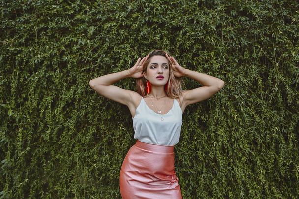 Hermosa joven mujer de moda en falda rosa y top azul de pie entre licencia verde
 - Foto, Imagen