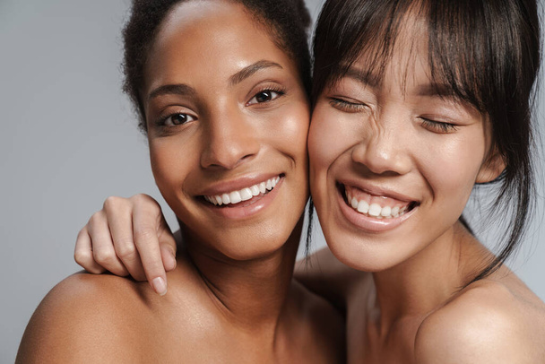 Portrait closeup of two multinational half-naked women hugging and laughing isolated over grey background - Fotografie, Obrázek