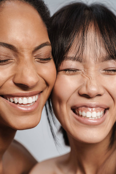 Portrait closeup of two multinational half-naked women hugging and laughing isolated over grey background - Foto, Bild