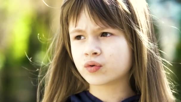 Portrait of pretty child girl with gray eyes and long fair hair smiling outdoors on blurred green bright background. Cute female kid on warm summer day outside. - Footage, Video
