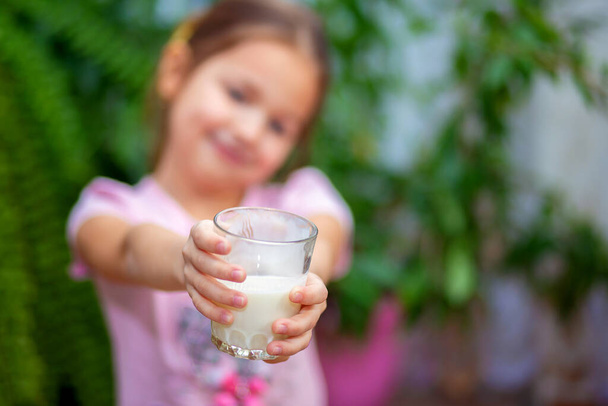 The girl holds forward a glass of kefir. Focus on the glass - Photo, image