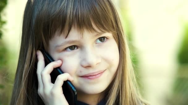 Portrét hezké holčičky s dlouhými vlasy mluvící na mobilu. Malá holčička komunikuje pomocí chytrého telefonu. Koncept dětské komunikace. - Záběry, video