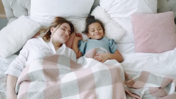Family in hurry to wake up quickly to fulfill their plans for day or idea come mind top-down view of bed by caring young mother mommy smiling lying on bed with joyful African American daughter - Video