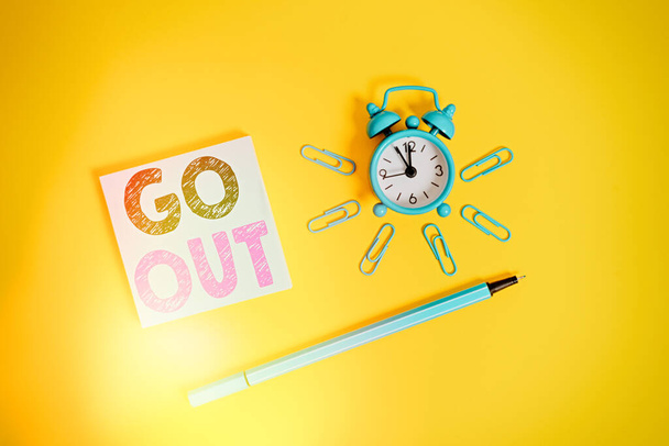 Writing note showing Go Out. Business photo showcasing to leave a room or building, especially in order to do something Metal alarm clock wakeup clips ballpoint notepad colored background. - Photo, Image