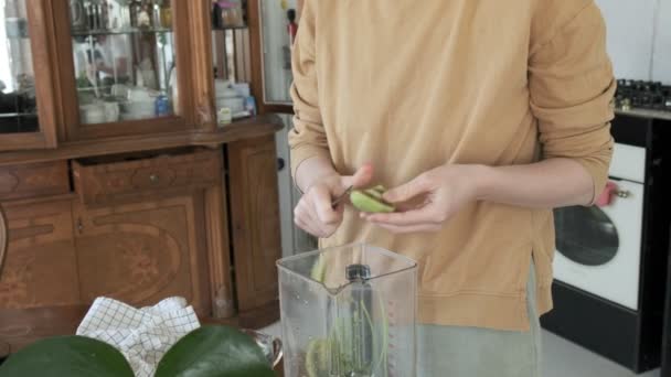 Dívka řeže kiwi nožem v kuchyni. mixér na stole. výroba koktejlů - Záběry, video