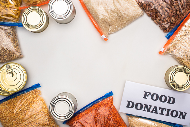 top view of cans and groats in zipper bags near card with food donation lettering on white background - Fotó, kép