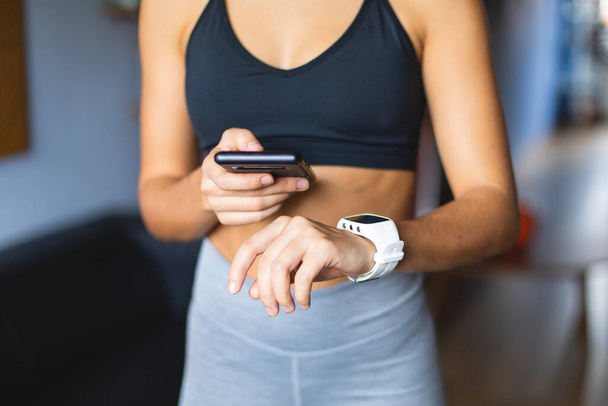 Entrenamiento de fitness en casa. Mujer joven en forma saludable utilizando smartphone y aplicación smartwatch para la formación
. - Foto, Imagen