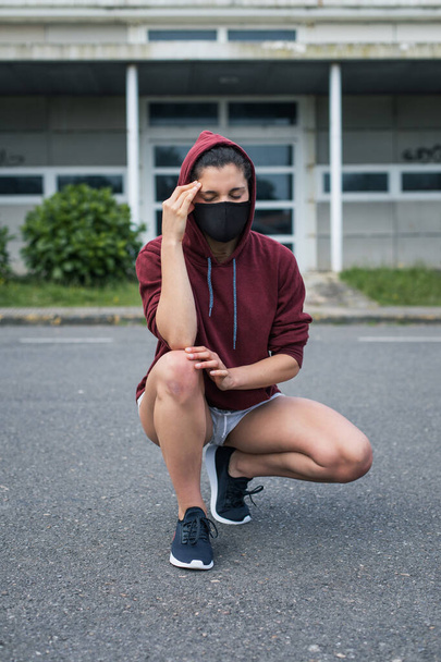 Female runner suffering headache. Sporty young woman wearing face mask for health protection under coronavirus crisis. Covid-19 symptom. - Foto, imagen