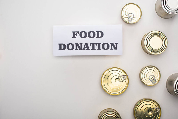 vista superior de latas cerca de la tarjeta con letras de donación de alimentos sobre fondo blanco
 - Foto, imagen