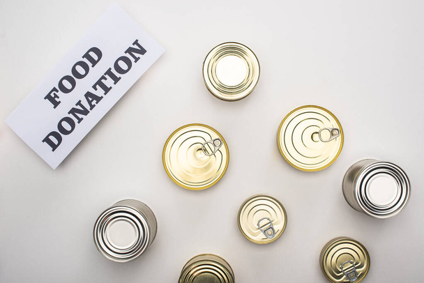 top view of cans with canned food on white background with food donation card - Φωτογραφία, εικόνα