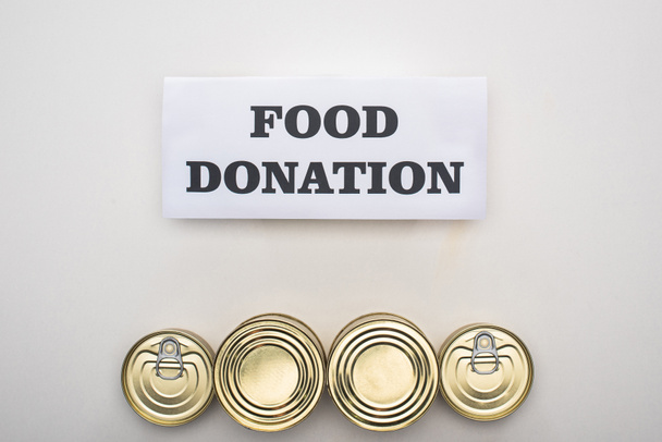 vista superior de latas com alimentos enlatados em fundo branco com cartão de doação de alimentos
 - Foto, Imagem