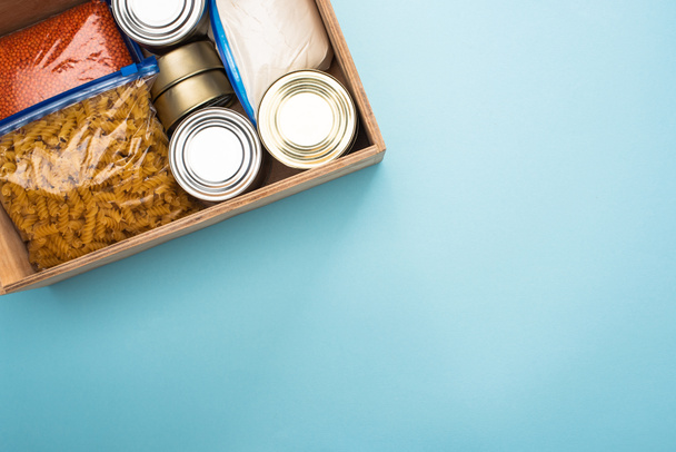 top view of cans and groats in zipper bags in wooden box on blue background - Photo, Image
