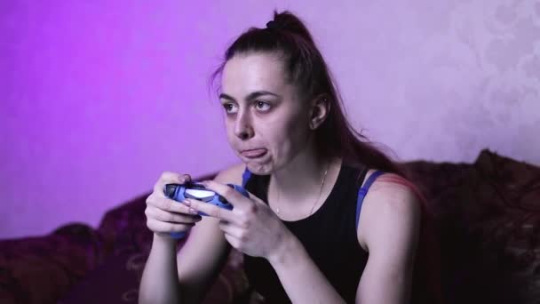 ικανοποιημένη gamer κορίτσι παίζει βιντεοπαιχνίδια κρατώντας ένα gamepad στα χέρια της και τρώει μάρκες στην καρέκλα. κόκκινα μαλλιά μιας γυναίκας σε απομόνωση στο σπίτι - Πλάνα, βίντεο