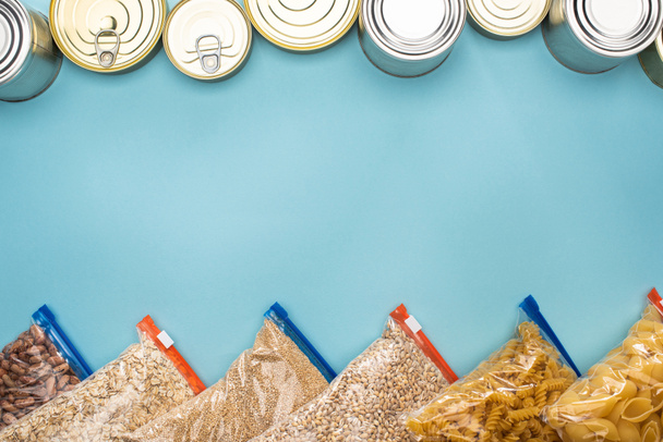 top view of cans, pasta and groats in zipper bags on blue background with copy space - Fotoğraf, Görsel