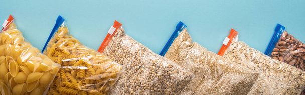 bovenaanzicht van pasta, bonen en gries in ritszakjes op blauwe achtergrond, voedseldonatie concept - Foto, afbeelding