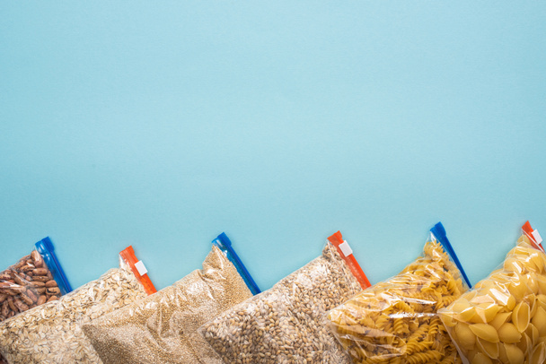 vista superior de massas, feijões e grumos em sacos de zíper no fundo azul, conceito de doação de alimentos
 - Foto, Imagem