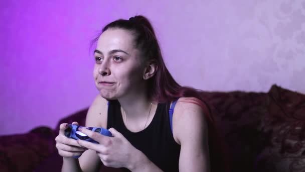 het meisje kauwt en lacht voor het scherm spelen van videospelletjes, likt smakelijke vingers, een tevreden gamer op de bank besteedt vrije tijd op isolatie - Video