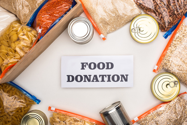 верхний вид банки и крупы в молнии мешки в деревянной коробке на белом фоне с картой пожертвования пищи
 - Фото, изображение
