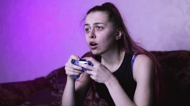 καταθλιπτικό κορίτσι στην απομόνωση παίζει βιντεοπαιχνίδια στο σπίτι στον καναπέ μπροστά από την τηλεόραση, κόκκινα μαλλιά και μεγάλα μάτια, φώτα νέον και συσκευές - Πλάνα, βίντεο
