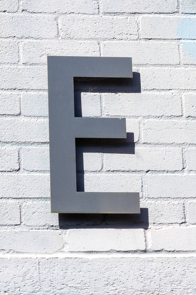 Písmeno e v kartáčované oceli na cihlové zdi s výrazným stínem - Fotografie, Obrázek