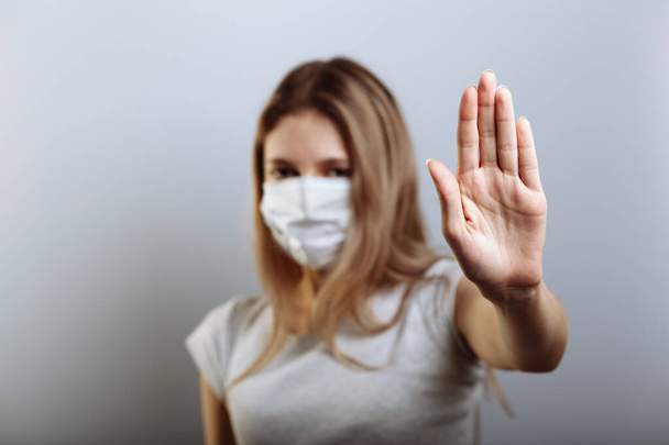 Frau mit Gesichtsmaske zeigt Stoppschild mit der Hand, um die Ausbreitung der Viren zu verhindern. Selektiver Fokus. - Foto, Bild
