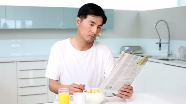 Attractive man eating cereal and reading magazine - Materiał filmowy, wideo