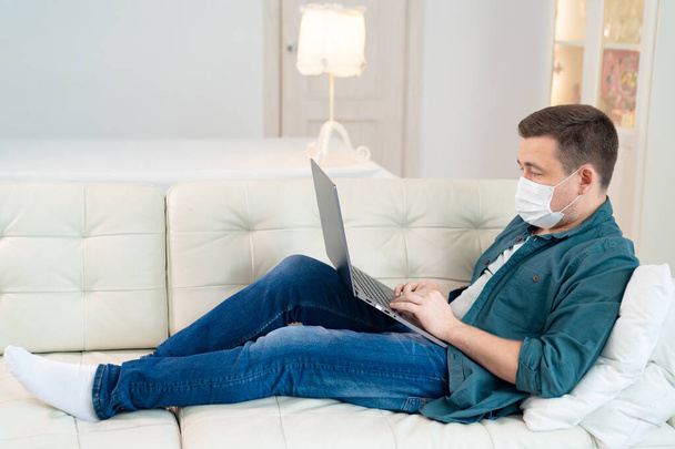 man blogger in medical mask working on couch - Fotó, kép