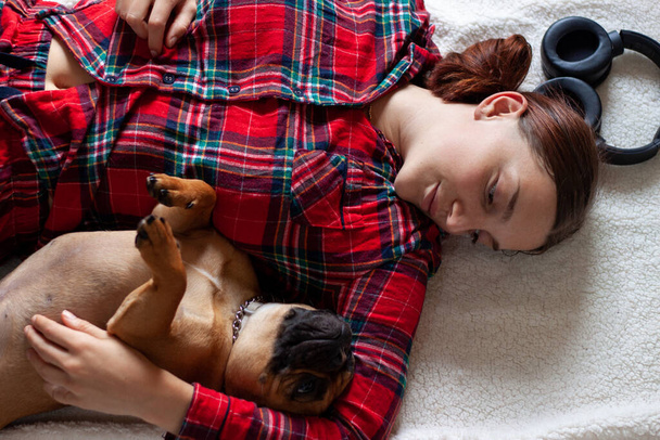 Evde yerde yatarken gülümseyen genç bir kadınla Fransız Bulldog. - Fotoğraf, Görsel