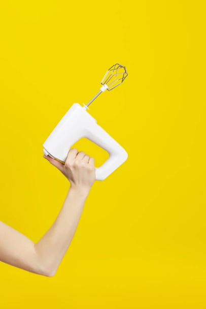 Misturador de cozinha branca na mão feminina isolado no fundo amarelo brilhante. Conceito de cozinha moderna
 - Foto, Imagem