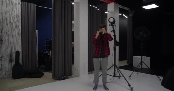Νεαρός όμορφος επαγγελματίας φωτογράφος φωτογραφίζει ένα μοντέλο σε ένα στούντιο. Είναι ευχαριστημένος με τις εικόνες που κατέγραψε. Ψηφιακή κάμερα DSLR. - Πλάνα, βίντεο