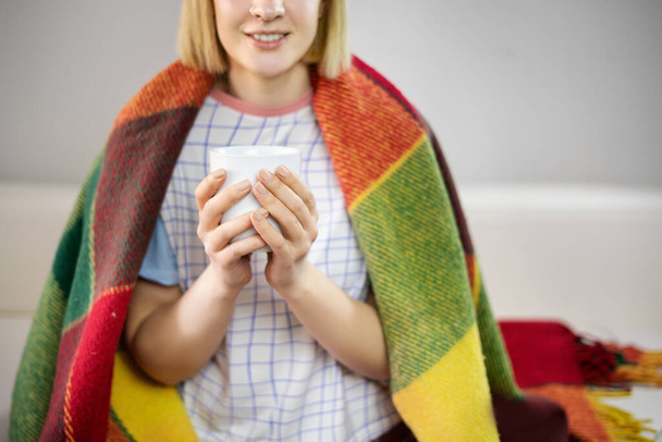 Girl wrapped in plaid with hot cup of tea in her hands. Copy space. - Photo, image