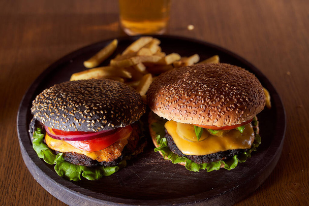 Two burgers dark and light leat on a wooden tray closeup photo - Photo, Image