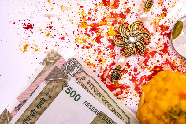 Индийский фестиваль Близкий вид разбросанных зерен риса, красный кумкум и куркум с элегантной ракхи, сладкие и индийские банкноты валюты на белой поверхности, традиционный индийский браслет запястья, который является символом любви
 - Фото, изображение