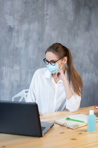 コロナウイルス。保護マスクを着用して自宅から働く若いビジネス女性。保護マスクを身に着けているコロナウイルスの隔離中のビジネス女性。サニタイザージェルで自宅から働く. - 写真・画像