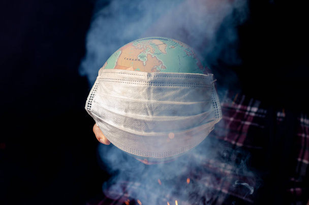 Peligro epidémico mundial. El mundo necesita proteger el globo terrestre con una máscara facial y manos, aisladas sobre un fondo negro. Peligro epidémico humano
. - Foto, imagen
